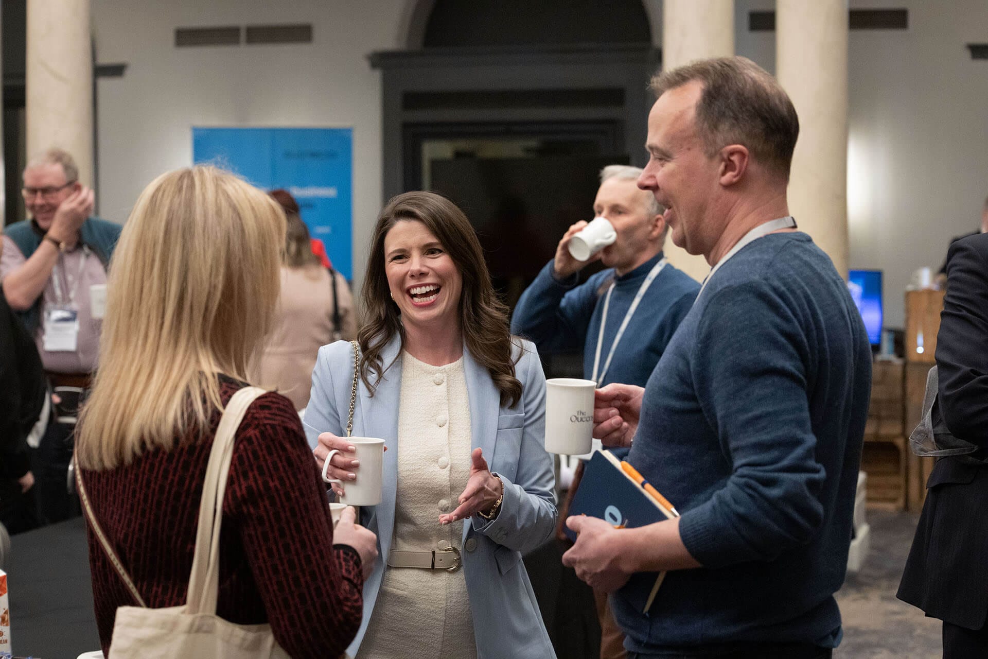 Three people chatting and smiling over coffee at a networking event.