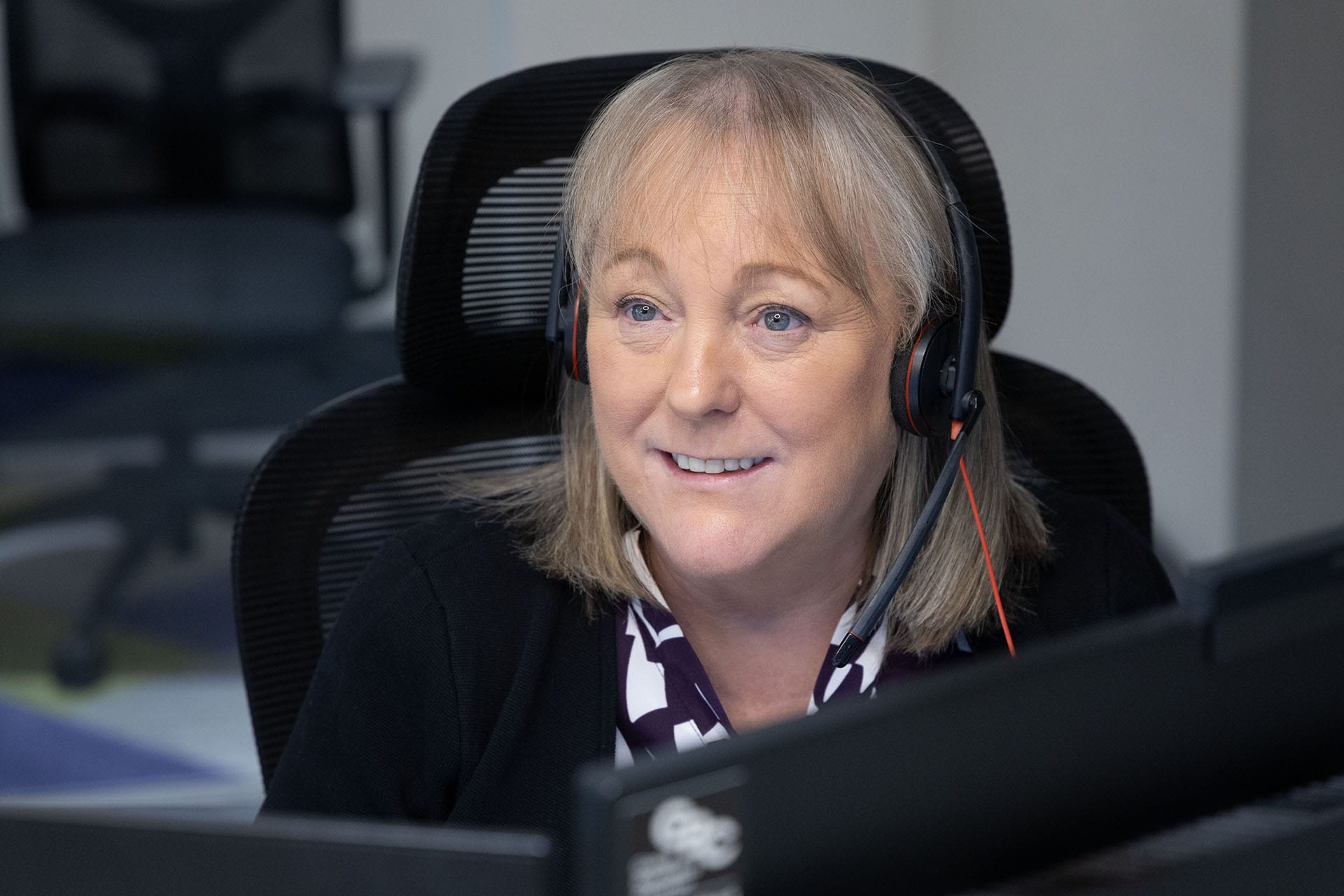 A woman wearing a headset smiles while working at her desk in an office.