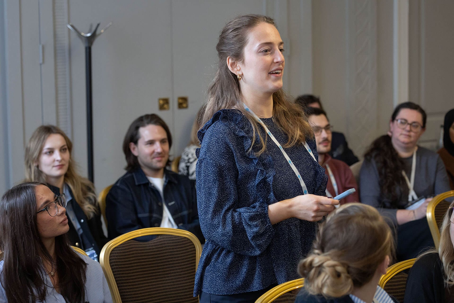 A woman standing and speaking during a workshop or panel session while attendees listen from their seats.
