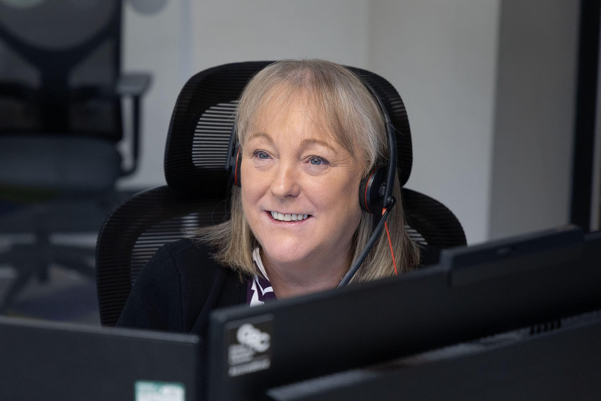 A woman wearing a headset smiles while working at her desk in an office.